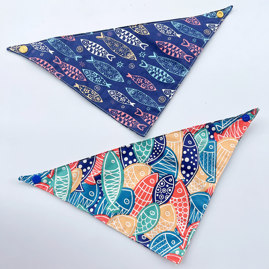 Navy and multicolor fish-pattern pet neckwear spread flat to show triangular bandana shapes and corner snaps