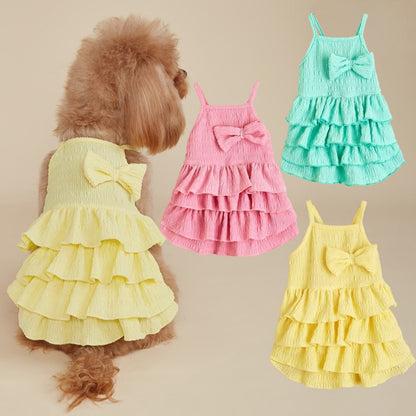 Small dog wearing Ozzie summer ruffle dress with bow, standing on wooden floor