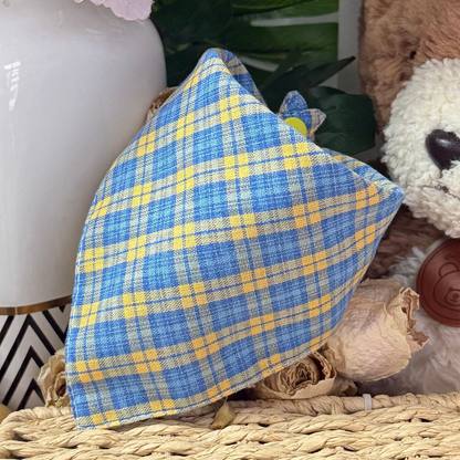 Blue plaid triangular pet neckwear with a yellow snap, displayed on a woven basket