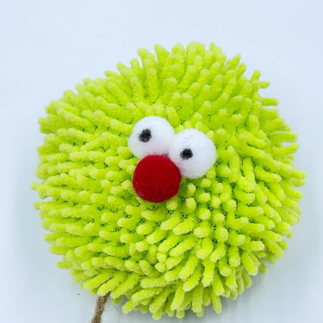 Close-up of the cat toy ball with green tufts, protruding white eyes and a red nose