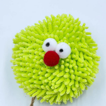 Close-up of the cat toy ball with green tufts, protruding white eyes and a red nose