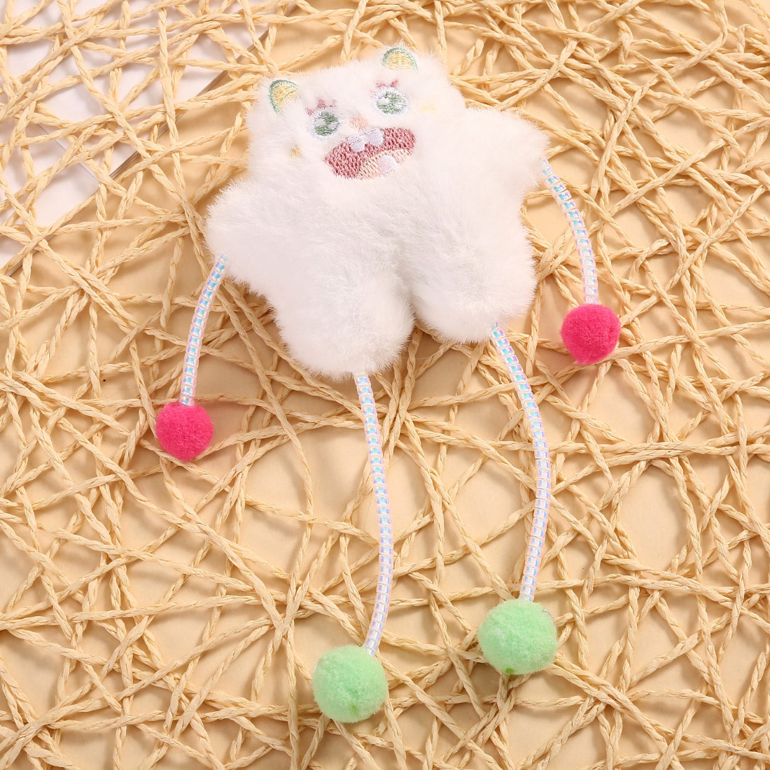 Moo cat toy hanging from a hand, featuring multiple pom poms