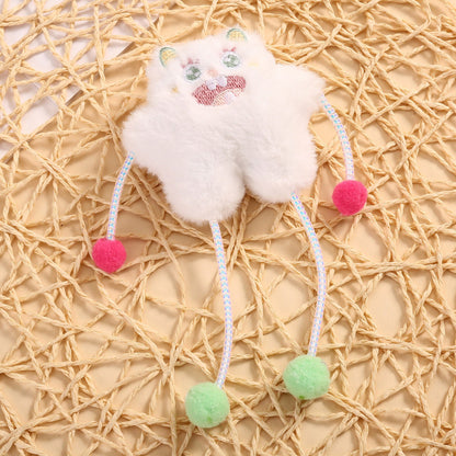 Moo cat toy hanging from a hand, featuring multiple pom poms