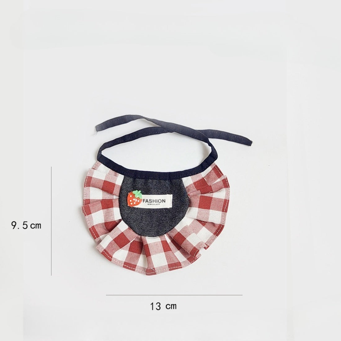 Cat wearing strawberry gingham bib sitting on wooden floor near a plant