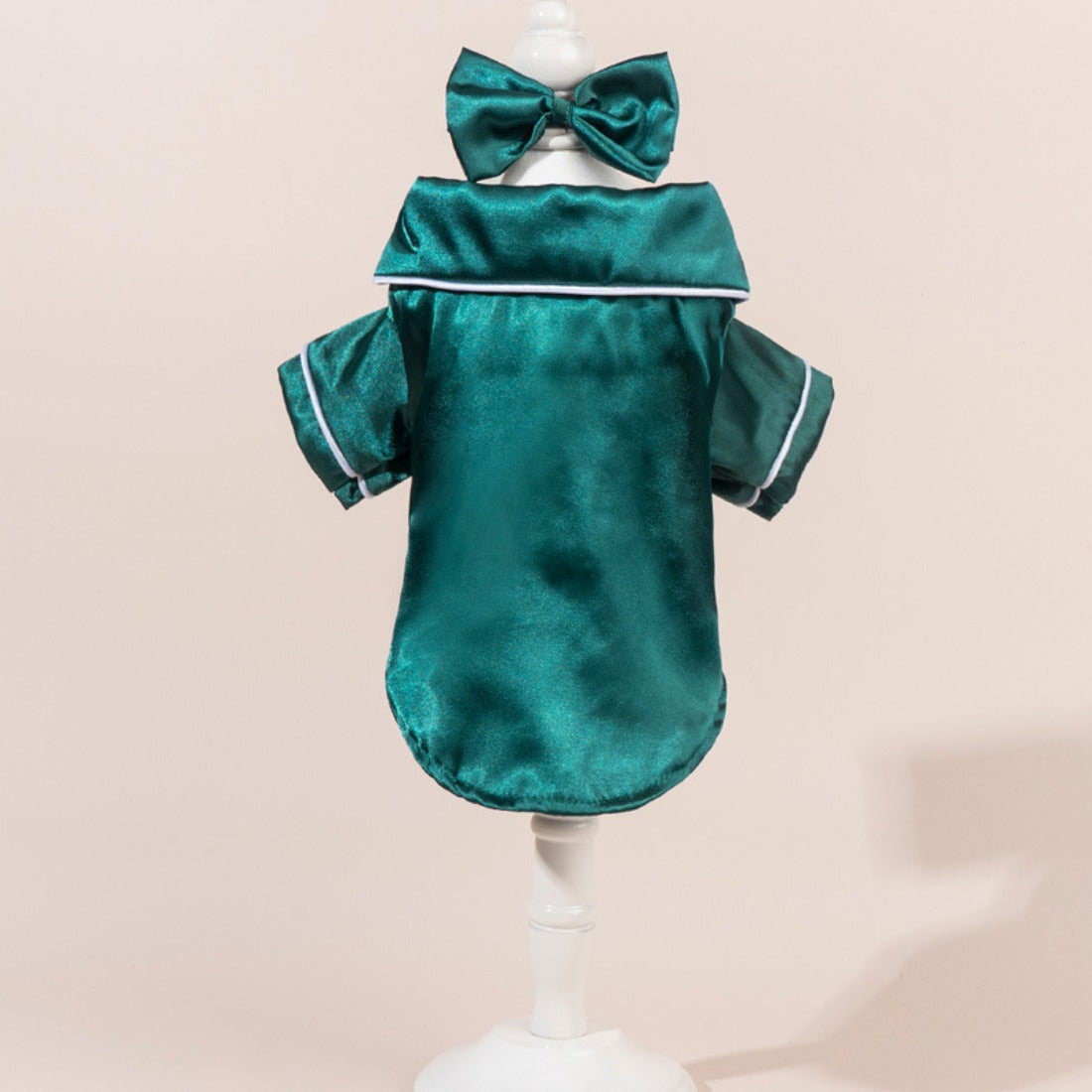 Small dog standing sideways wearing a shiny satin shirt with a bow