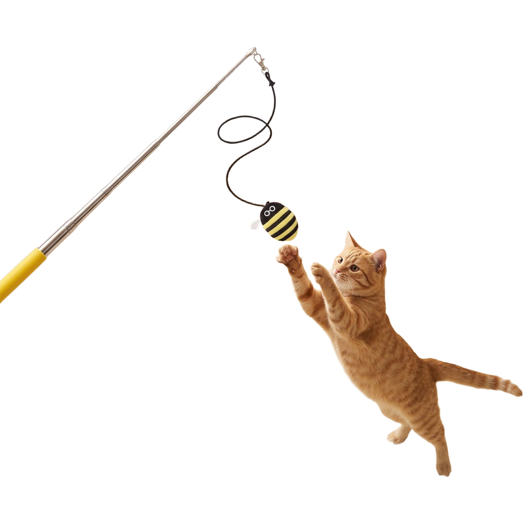 Cat reaching toward a suspended bee attachment on a yellow-handled cat teaser wand