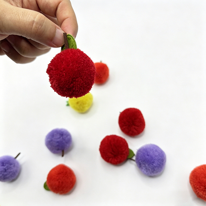 Hand holding a red fruit-shaped ball cat toy by its stem beside a green leaf