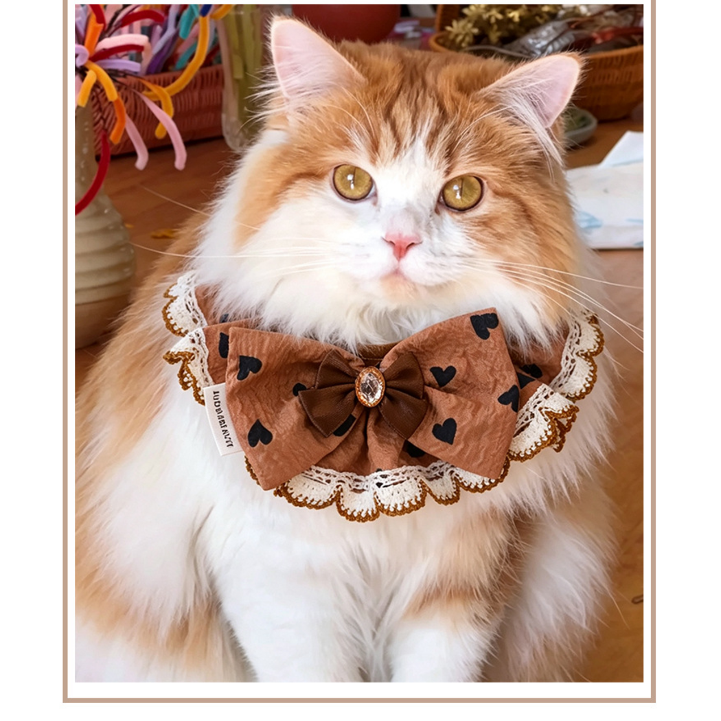 Hearts Pet Neckwear with a layered brown bow and scalloped edging, worn by an orange-and-white cat