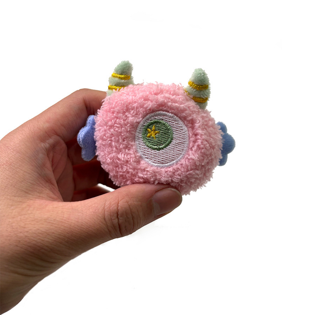 Pink one-eyed cat toy held between fingers