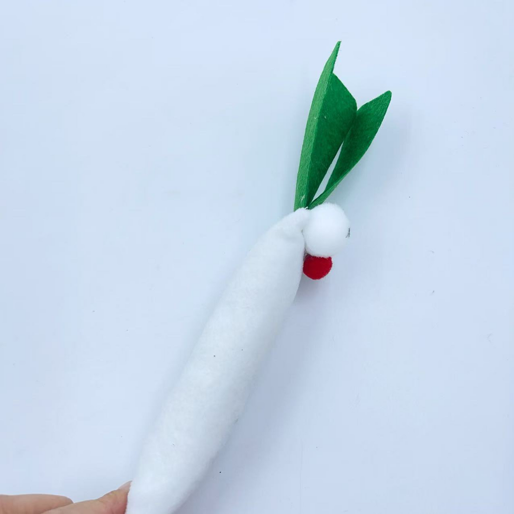 Side detail of the scallion-shaped cat toy held at the lower edge, showing projecting eyes, red nose and green leaves
