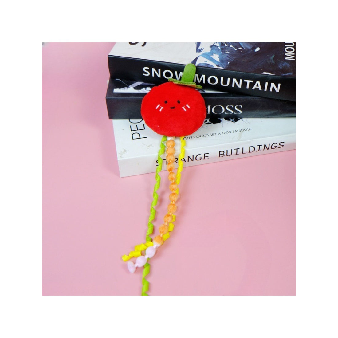 Moo fruit plush cat toy with ribbons placed next to a small plant