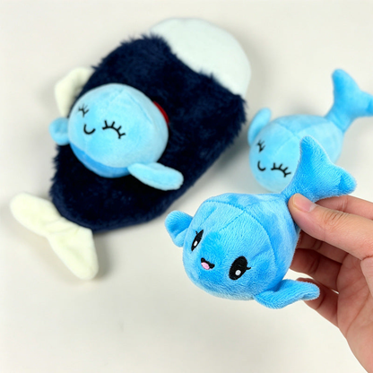 Hand holding a light blue dolphin-shaped plush toy, with a dark whale-shaped plush in the background
