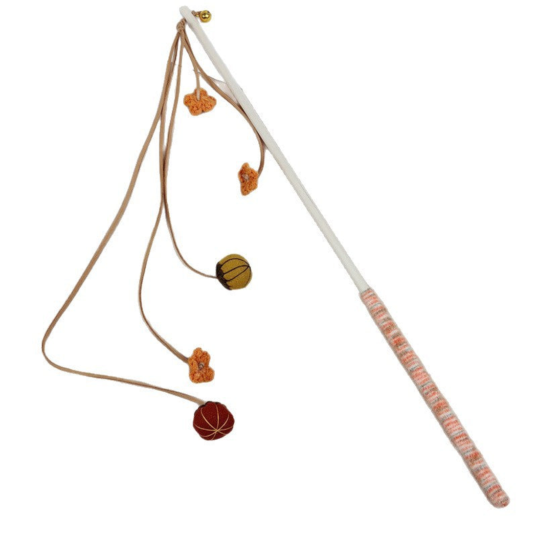 Pumpkin cat teaser wand with brown cords, orange flowers, rounded ornaments, and a striped handle on white.