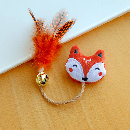 Fox cat toy with an embroidered face, braided cord, gold-colored bell and orange spotted feathers.