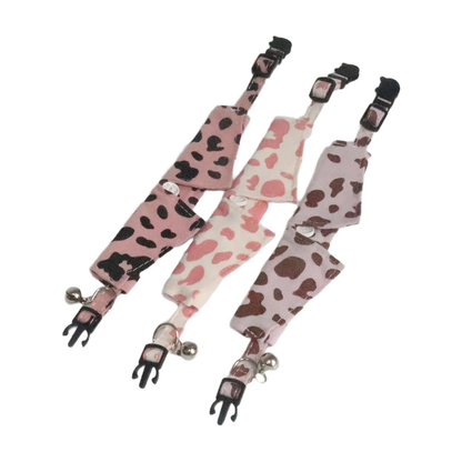 Three cow-print pointed cat collars laid open to show the straps, buckles and bells