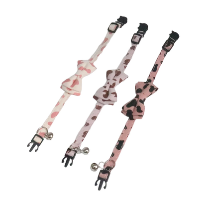 Three cow-print bow tie cat collars laid open to show the adjustable straps and bells