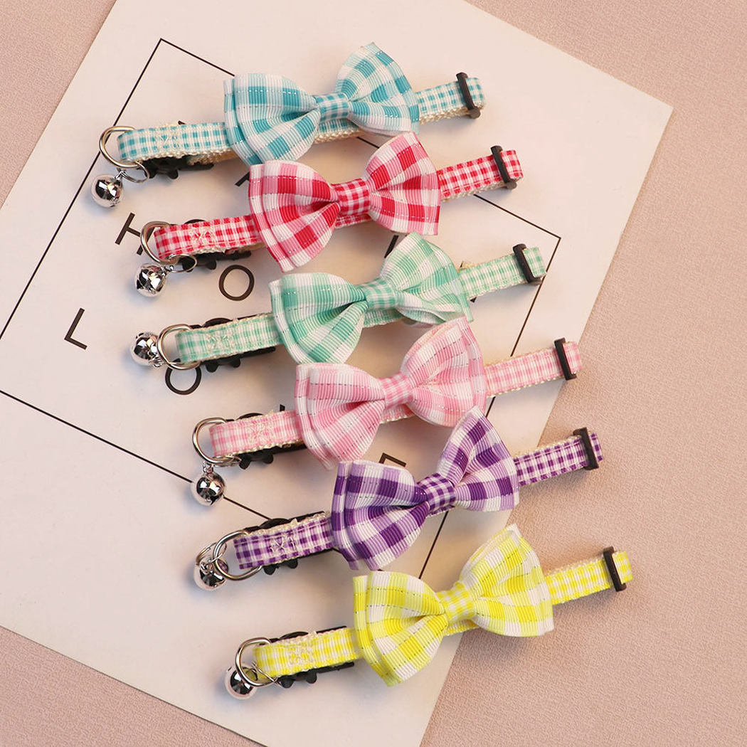 Six gingham bow cat collars with bells arranged on a pale pink background