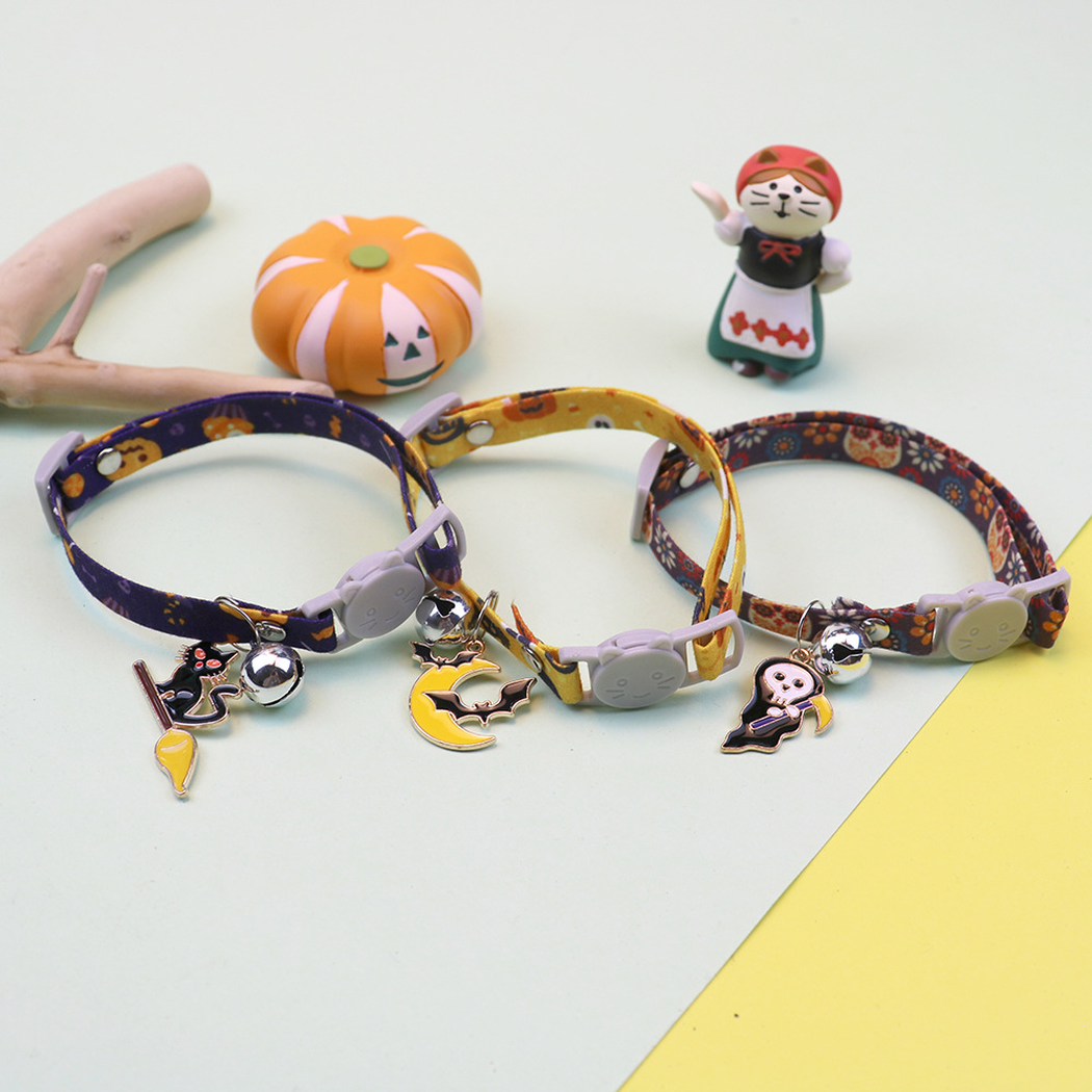 Three Halloween cat collars arranged with pumpkin and figurine decorations