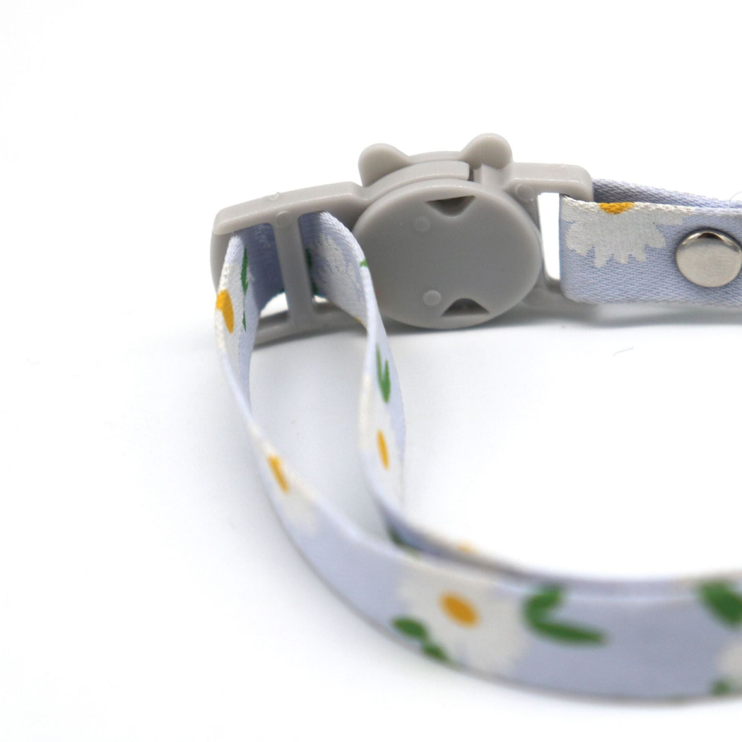 Close-up of the cat-face buckle and threaded daisy-print collar strap