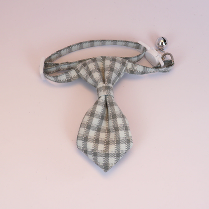 Gray-blue plaid cat collar with necktie-shaped bow, white buckle and silver-tone bell