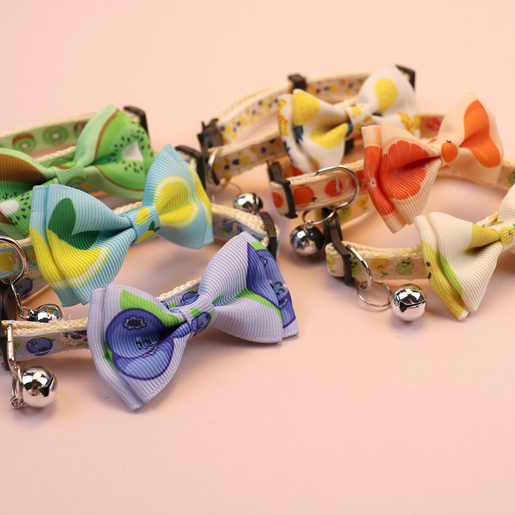 Close-up of fruit-print cat collars with bows, bells and buckle hardware