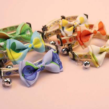 Close-up of fruit-print cat collars with bows, bells and buckle hardware
