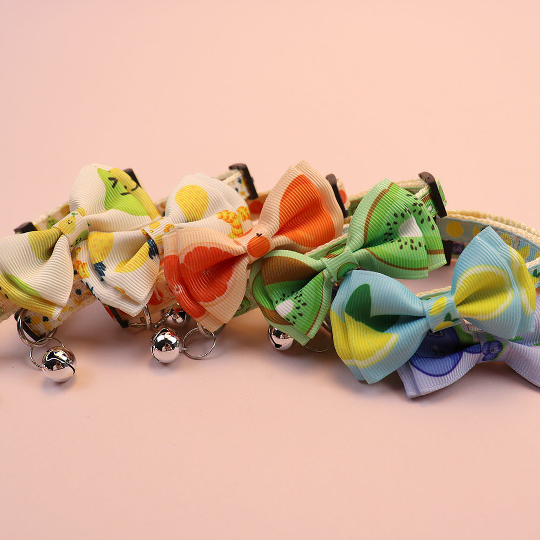 Assorted fruit-print cat collars arranged in a row with bows and bells