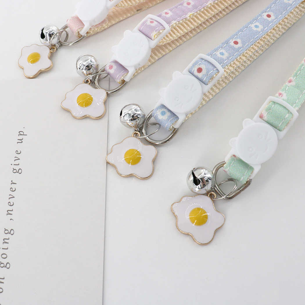 Close-up of cat-face buckles, bells and fried egg charms on four collars