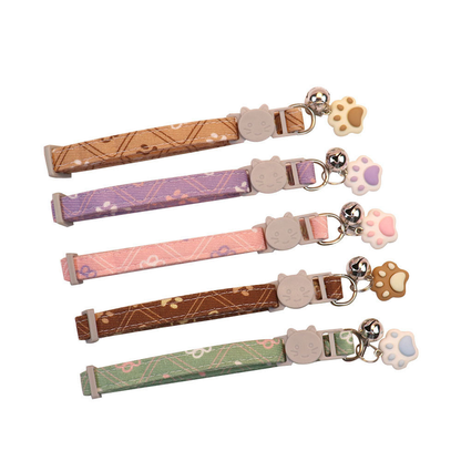 Five patterned cat collars with bells and paw-shaped charms on a white background