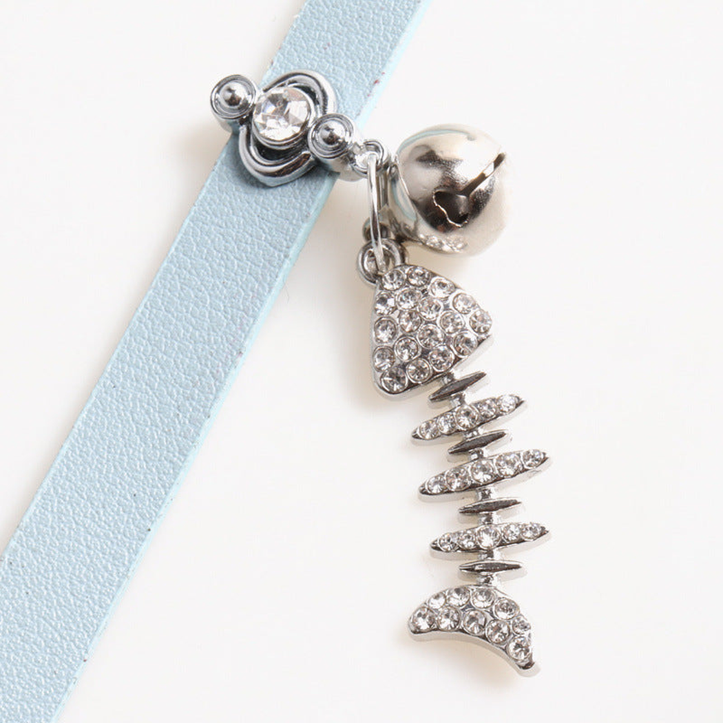 Close-up of the bell and clear-accented fishbone charm on a light blue cat collar