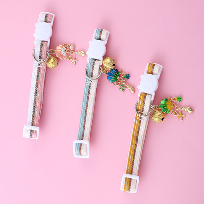 Pink, light blue and mustard yellow striped cat collars laid flat with dangling charms