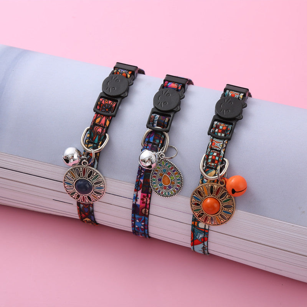 Three multicolor cat collars with bells and hanging medallions displayed together