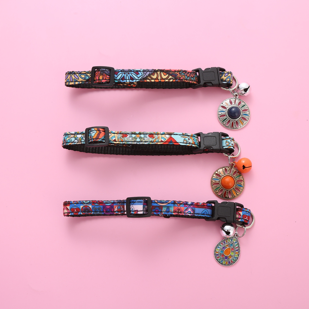 Three adjustable multicolor cat collars laid flat with buckles, bells and medallions