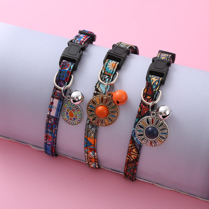 Three patterned cat collars with black buckles, bells and hanging medallions