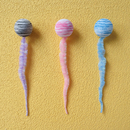 Gray, pink, and blue striped ball-and-tail cat toys arranged in a row
