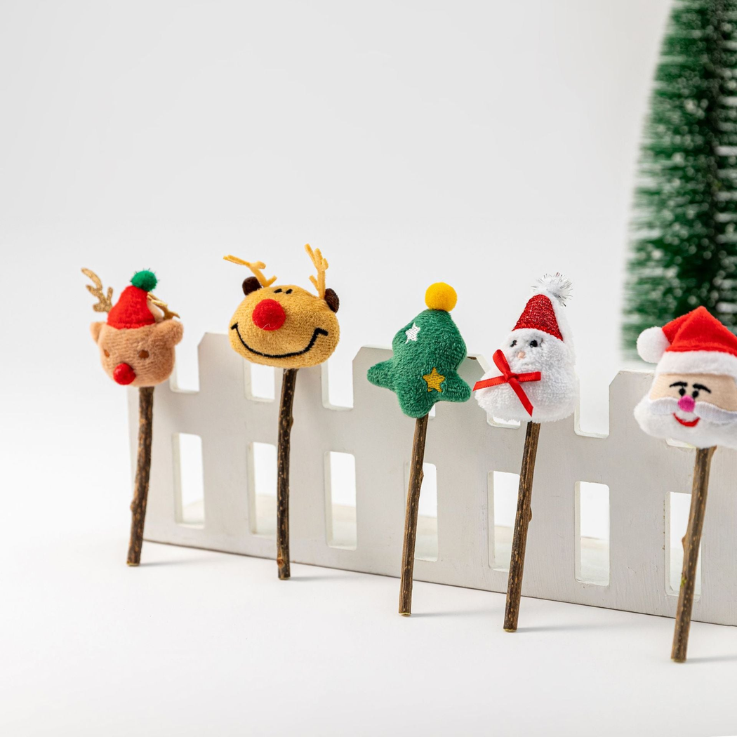 Five Christmas character stick cat toy styles displayed beside a white fence