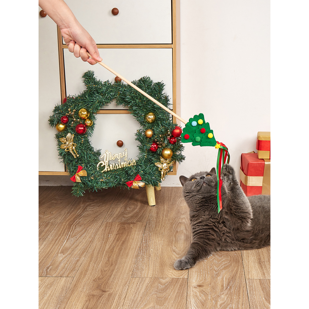 Cat reaching for a Christmas tree teaser wand beside holiday decorations