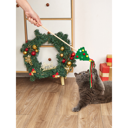 Cat reaching for a Christmas tree teaser wand beside holiday decorations