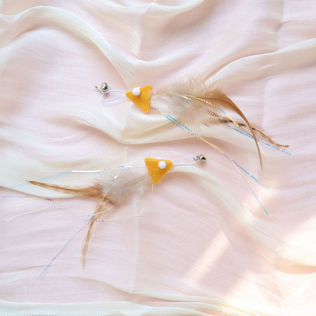 Two yellow fish-shaped cat teaser replacement attachments arranged on pink fabric