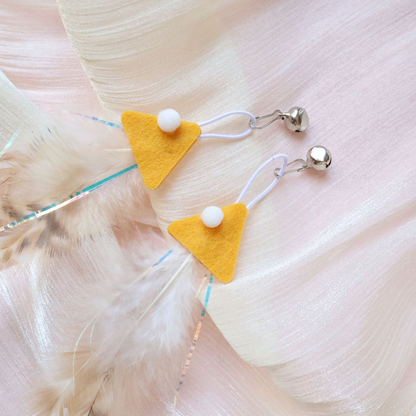 Close-up of yellow fish-shaped attachments with white pom-poms, cord loops and silver-tone bells