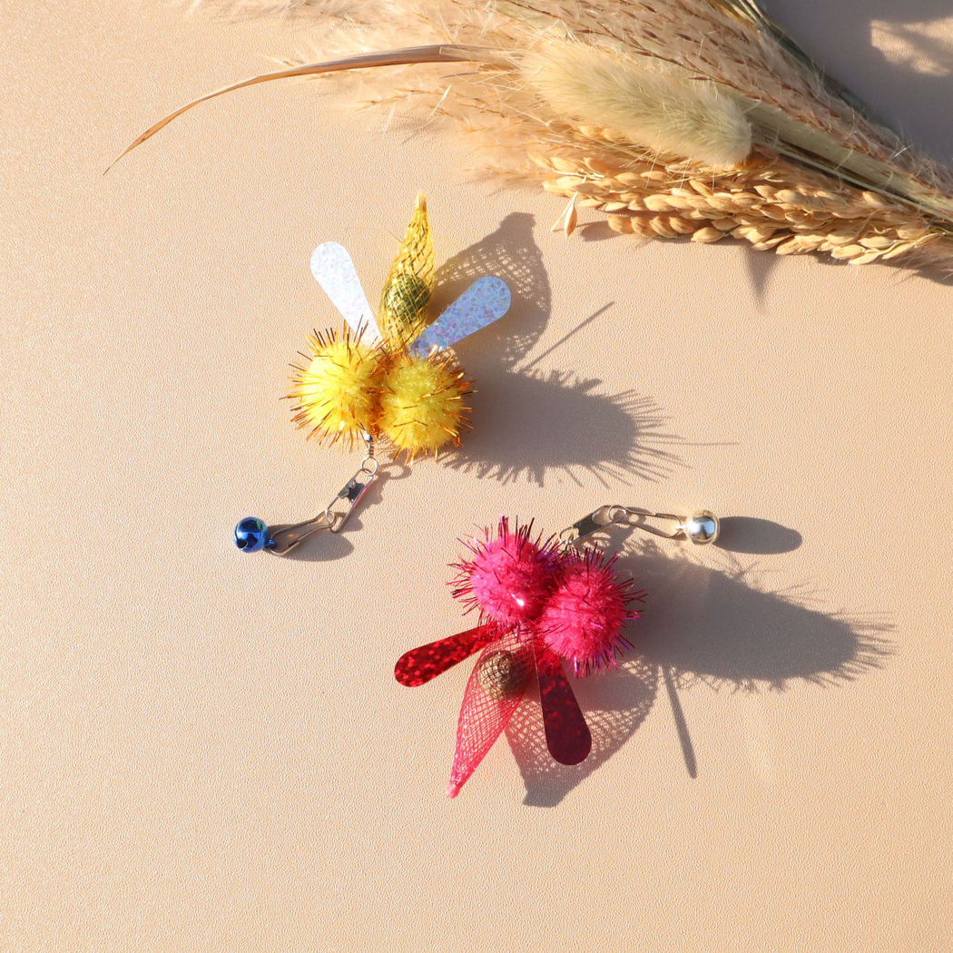 Yellow and fuchsia winged cat toy attachments displayed with their clips and bells