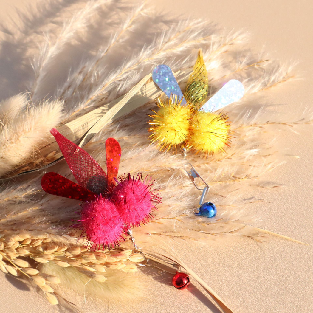 Fuchsia and yellow winged cat toy attachments nestled among dried grasses