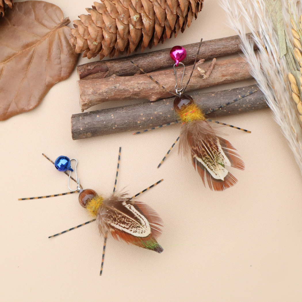 Two winged insect-shaped cat toys arranged with branches, a pine cone and dried foliage