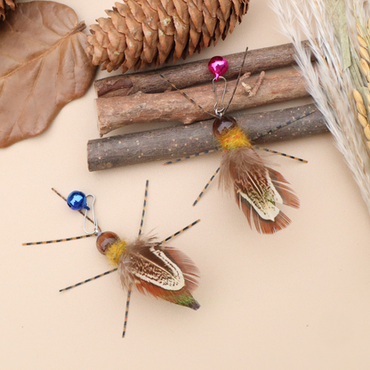 Two winged insect-shaped cat toys arranged with branches, a pine cone and dried foliage
