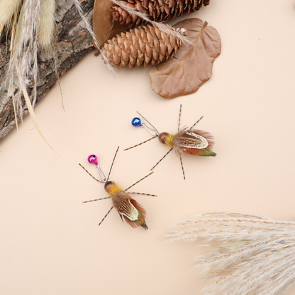 Two winged insect-shaped cat toys arranged among pine cones, bark and dried grasses