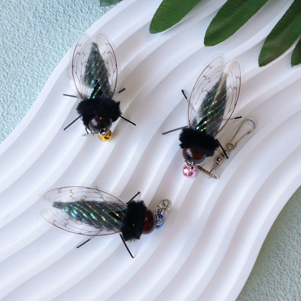 Three cicada-shaped cat toy attachments displayed with colored bells and clasps