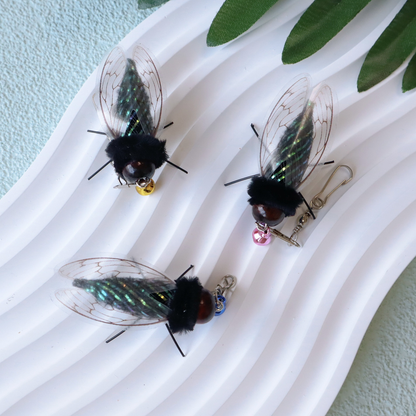 Three cicada-shaped cat toy attachments displayed with colored bells and clasps