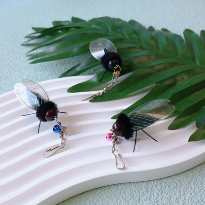 Three cicada-shaped cat toy attachments arranged with leafy props