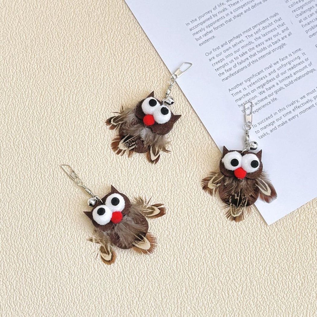 Three owl-shaped cat toy attachments arranged beside an open book