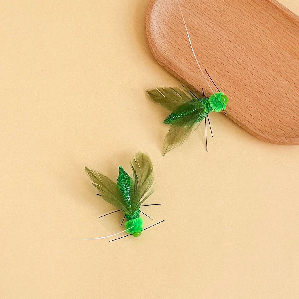 Two green winged insect-shaped cat toy attachments beside a rounded wood-look prop